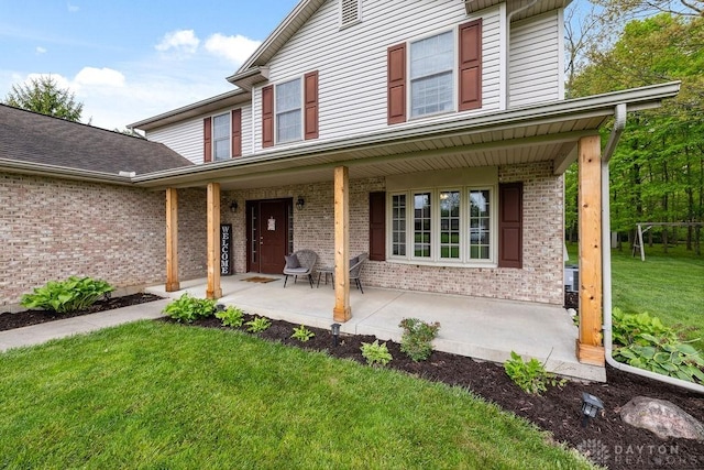 property entrance featuring brick siding, a porch, and a lawn