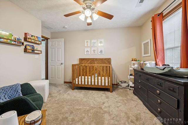 carpeted bedroom featuring a nursery area, a ceiling fan, and baseboards