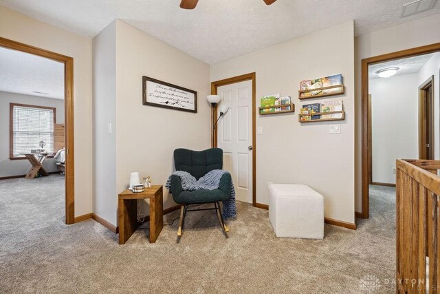 living area with light colored carpet, a ceiling fan, baseboards, and a textured ceiling