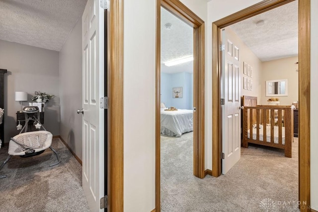 hall with a textured ceiling, carpet floors, and baseboards