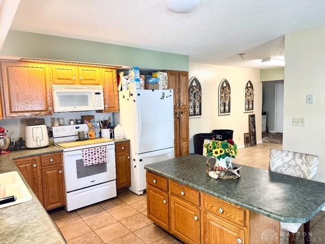 kitchen featuring white appliances, light tile patterned flooring, a kitchen island, and brown cabinets