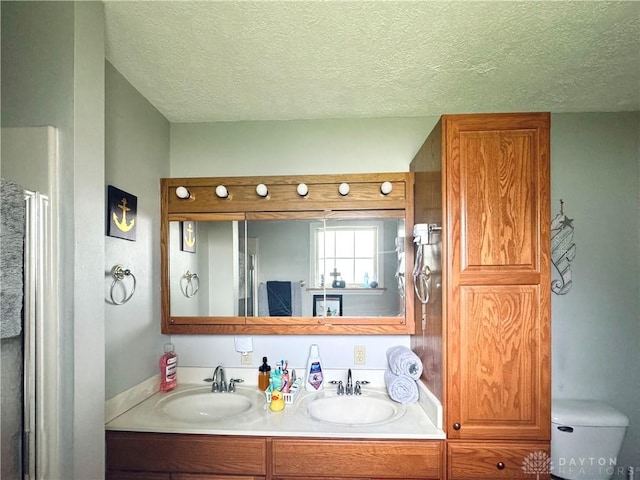bathroom with a textured ceiling, double vanity, and toilet