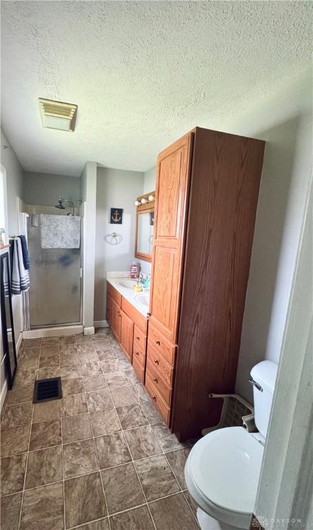 full bath with a stall shower, toilet, vanity, a textured ceiling, and baseboards