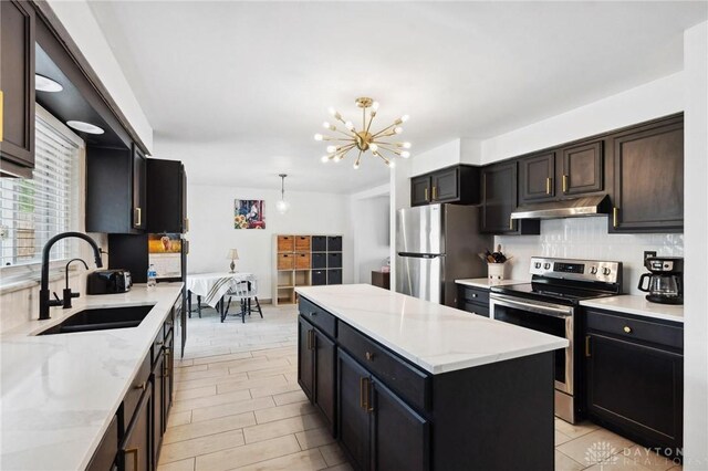 kitchen with stainless steel appliances, a sink, decorative backsplash, under cabinet range hood, and a center island
