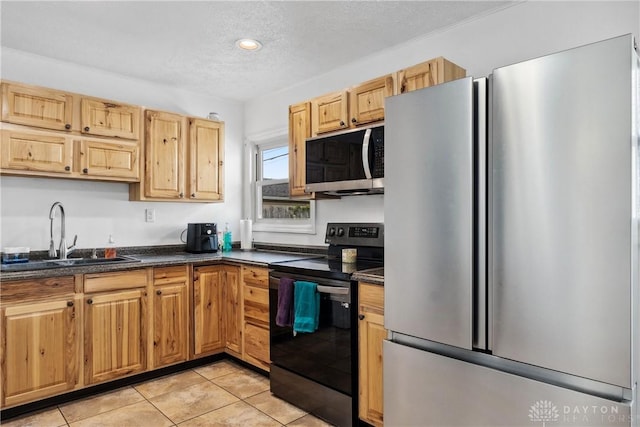 kitchen with appliances with stainless steel finishes, a sink, dark countertops, light tile patterned floors, and a textured ceiling
