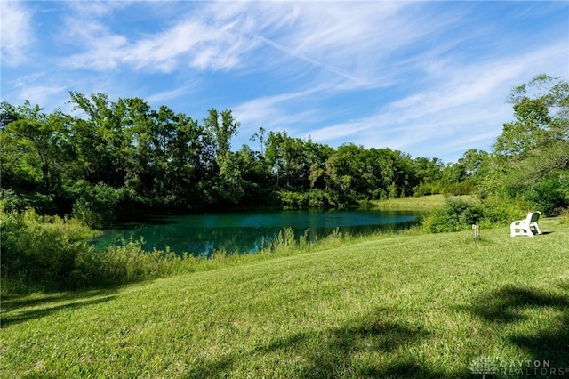 view of green lawn with a water view and a forest view