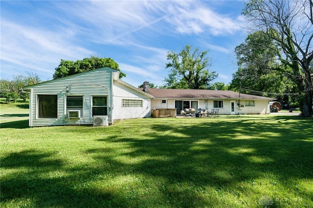 back of property featuring a hot tub, a lawn, a chimney, and a patio