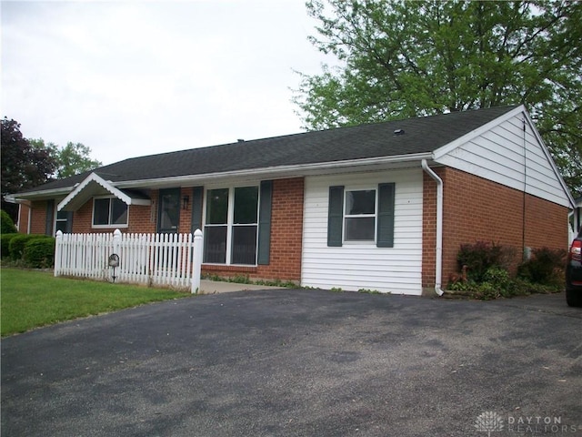 ranch-style home featuring brick siding, fence, and asphalt driveway