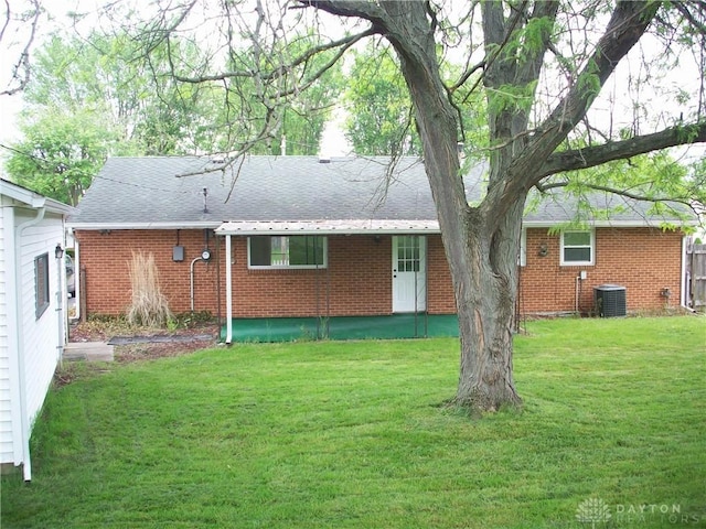 rear view of property with a lawn, brick siding, cooling unit, and a shingled roof