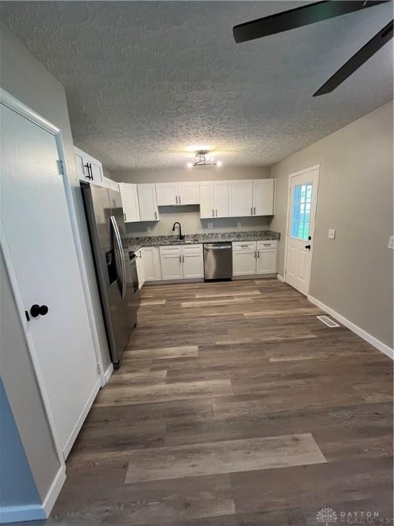 kitchen featuring stainless steel appliances, a ceiling fan, white cabinetry, a sink, and dark wood-type flooring