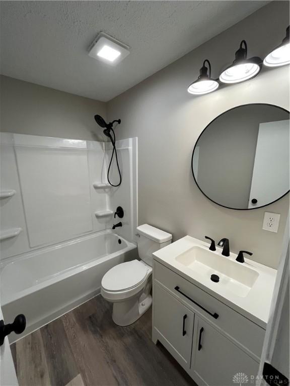 full bath featuring wood finished floors, toilet, shower / washtub combination, vanity, and a textured ceiling