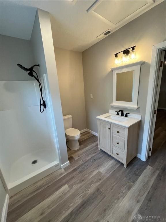 bathroom featuring toilet, a shower, wood finished floors, vanity, and baseboards