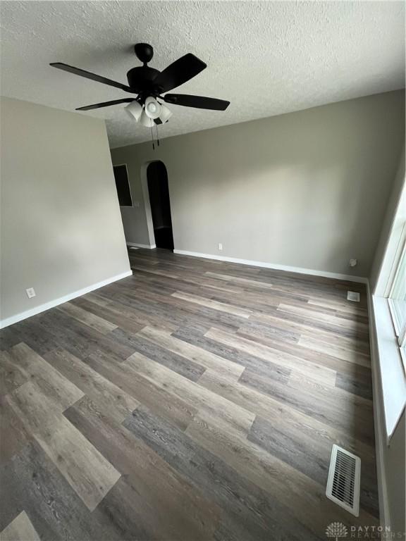 spare room with arched walkways, a ceiling fan, baseboards, wood finished floors, and a textured ceiling