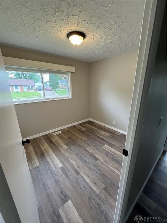 unfurnished room featuring a textured ceiling, wood finished floors, and baseboards