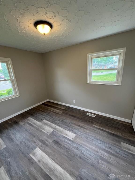 empty room with healthy amount of natural light, dark wood-style flooring, and a textured ceiling
