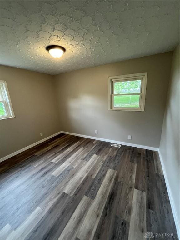 spare room with plenty of natural light, dark wood-style flooring, baseboards, and a textured ceiling