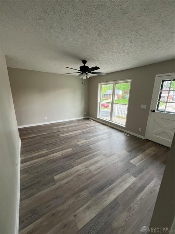 empty room with a textured ceiling, ceiling fan, baseboards, and wood finished floors
