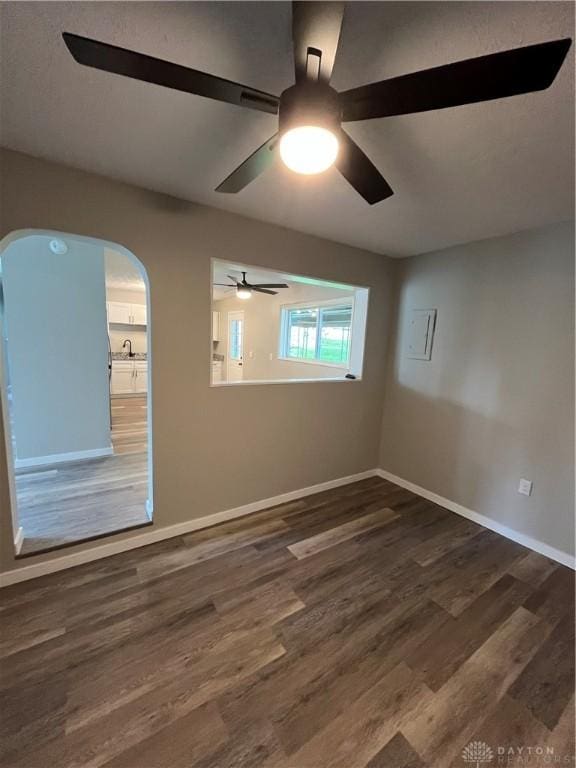 spare room with arched walkways, wood finished floors, ceiling fan, and baseboards