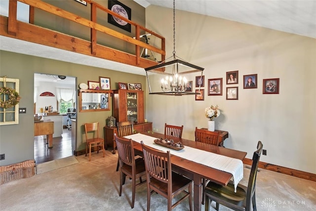 carpeted dining area with a chandelier, high vaulted ceiling, and baseboards