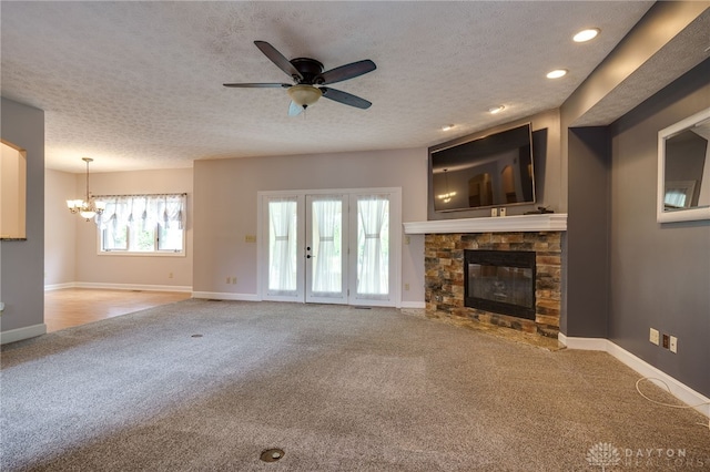 unfurnished living room with carpet, a chandelier, a ceiling fan, a fireplace, and a textured ceiling