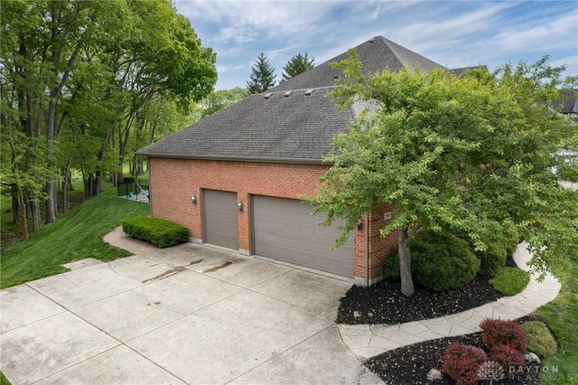 view of home's exterior featuring roof with shingles, brick siding, driveway, a yard, and an attached garage