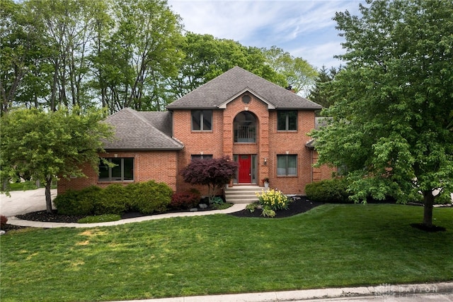 view of front of house with roof with shingles, a front yard, and brick siding
