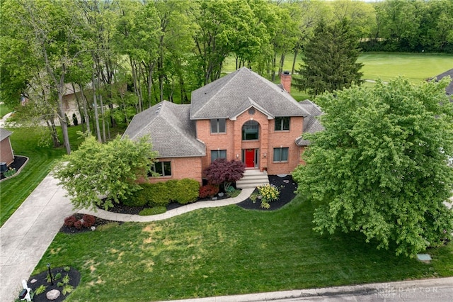 colonial home featuring brick siding, a front lawn, a chimney, and roof with shingles