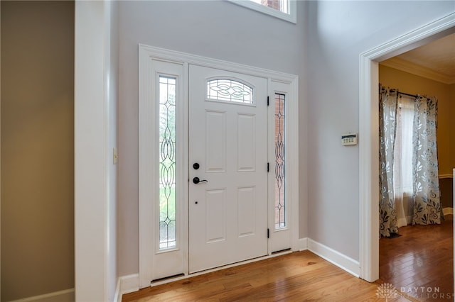 foyer with light wood-style floors, baseboards, and crown molding