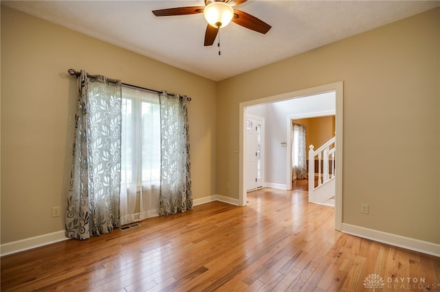 unfurnished room with a ceiling fan, wood-type flooring, stairs, and baseboards