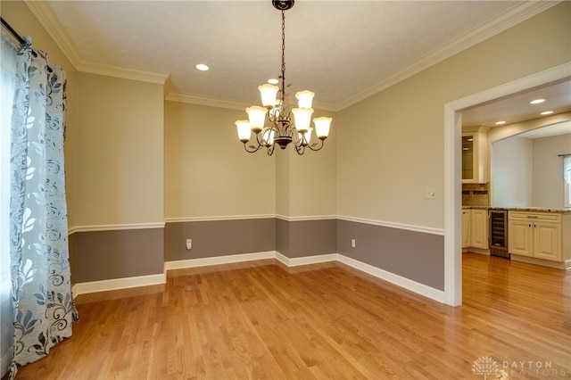 spare room with wine cooler, light wood-style flooring, ornamental molding, baseboards, and a chandelier