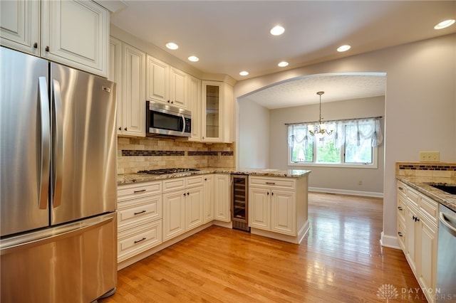 kitchen featuring appliances with stainless steel finishes, wine cooler, tasteful backsplash, light wood-type flooring, and baseboards