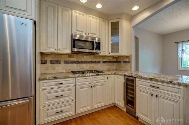 kitchen featuring appliances with stainless steel finishes, wine cooler, light stone counters, backsplash, and recessed lighting