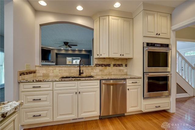 kitchen with stainless steel appliances, a sink, ceiling fan, light stone countertops, and backsplash