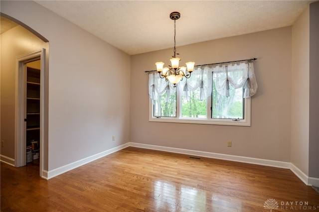 spare room featuring arched walkways, a chandelier, wood finished floors, and baseboards