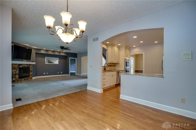 unfurnished living room featuring arched walkways, a chandelier, a sink, a stone fireplace, and baseboards