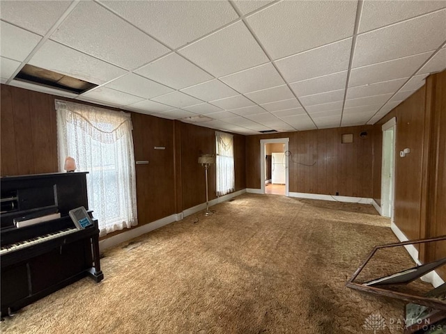 318 E Main St, Bradford, OH 45308 - unfurnished living room featuring light carpet, a paneled ceiling, wood walls, healthy amount of natural light, and baseboards