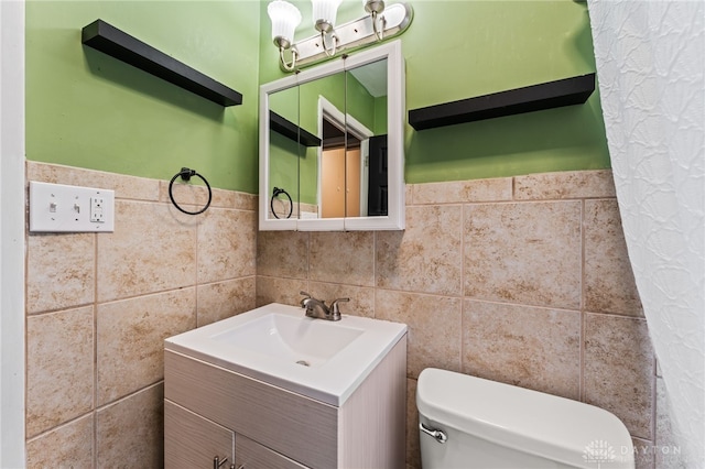 half bathroom featuring tile walls, toilet, vanity, and a wainscoted wall
