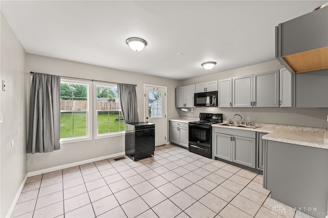 kitchen with black appliances, gray cabinets, light countertops, a sink, and baseboards