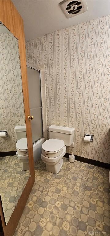 bathroom with toilet, tile patterned floors, and bath / shower combo with glass door