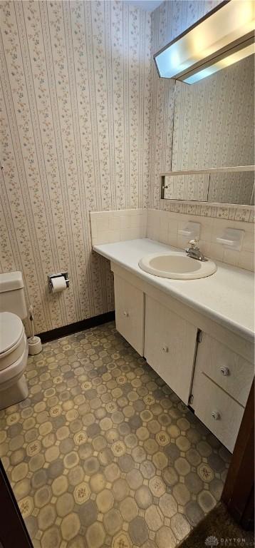half bathroom with vanity, tile patterned floors, toilet, and wallpapered walls