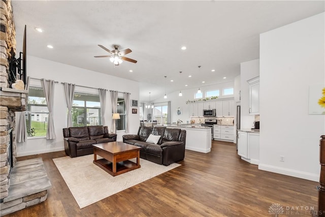 living room with a ceiling fan, a stone fireplace, dark wood-style floors, recessed lighting, and baseboards