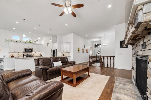 living room featuring a ceiling fan, dark wood finished floors, a fireplace, recessed lighting, and a chandelier