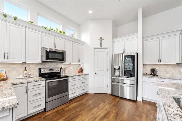 kitchen with stainless steel appliances, white cabinets, tasteful backsplash, dark wood finished floors, and light stone countertops