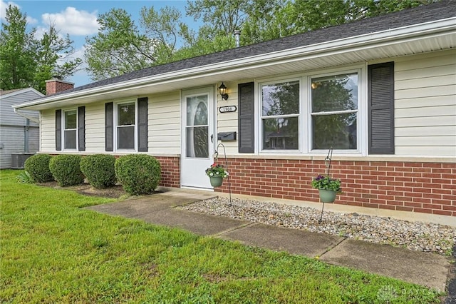 view of front facade with brick siding, a front yard, central AC, and a chimney
