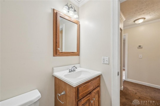 half bath with toilet, vanity, ornamental molding, a textured ceiling, and baseboards