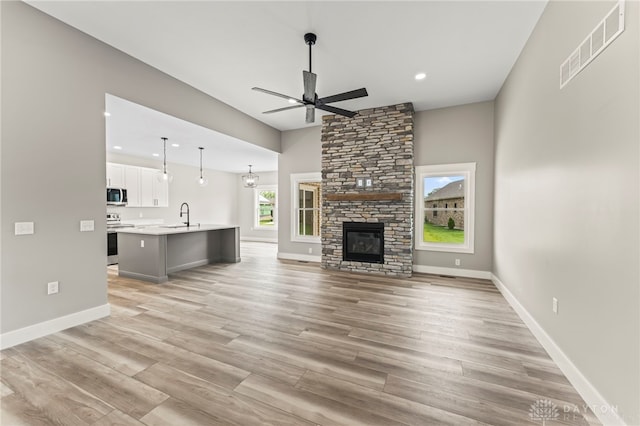 755 W Bentley Cir, Troy, OH 45373 - unfurnished living room with a ceiling fan, a fireplace, light wood-style flooring, recessed lighting, and a sink