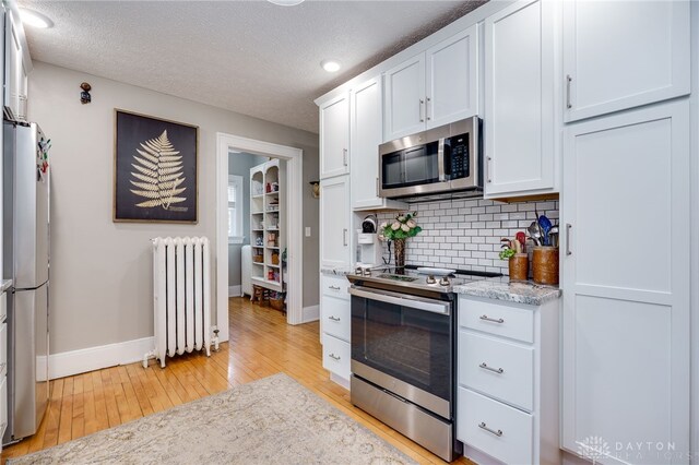 65 N Central Ave, Fairborn, OH 45324 - kitchen featuring appliances with stainless steel finishes, light wood-style floors, radiator heating unit, backsplash, and white cabinets