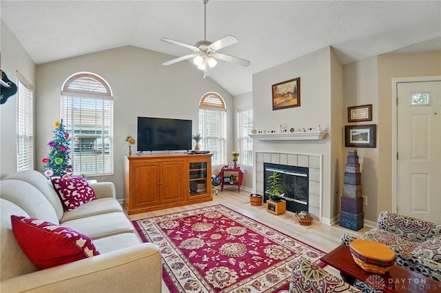 living area featuring a ceiling fan, light wood finished floors, a fireplace, vaulted ceiling, and baseboards