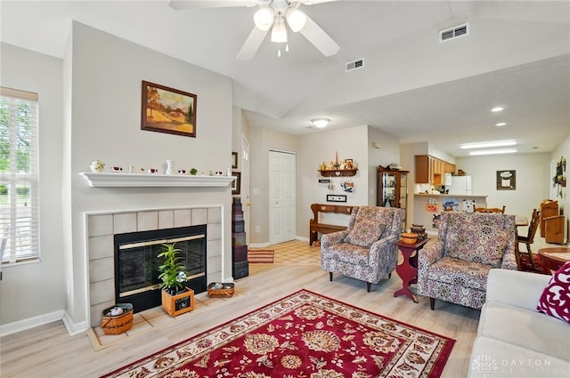 living room with vaulted ceiling, a tiled fireplace, light wood-style floors, a ceiling fan, and baseboards