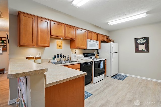 kitchen featuring a sink, white appliances, a peninsula, and light wood finished floors